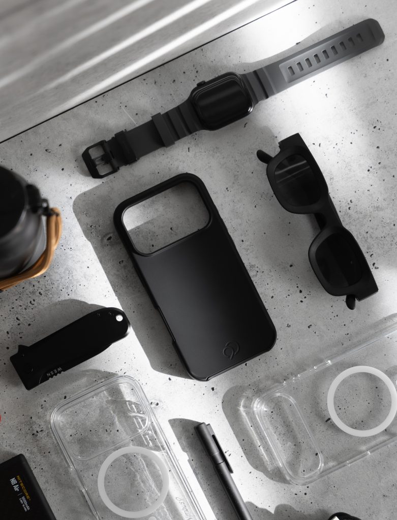 Flat-lay of Nimbus9 iPhone 17 case and accessories on a workbench, in monochrome, highlighting slim MagSafe-ready design.